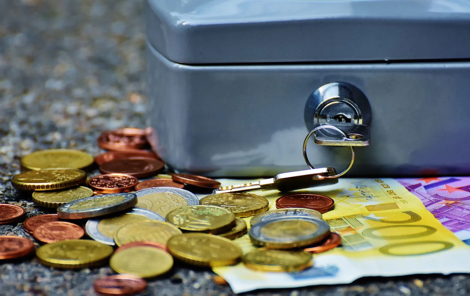 Banknotes and coins beside a metal cash box